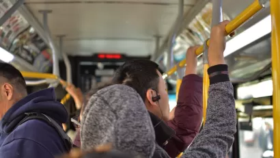 Interior of busy city bus with people standing, holding on to top bar.