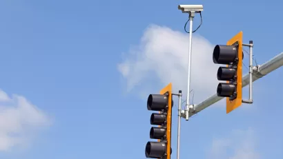 Yellow and black stoplights on horizontal post with small traffic camera.