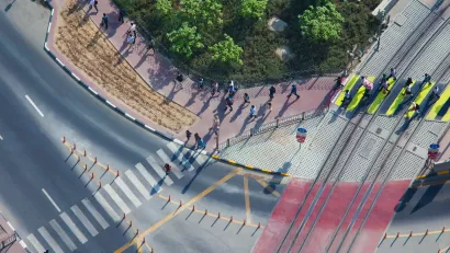 Overhead view of doxens of commuters walking on sidewalk and crossing street in full sun.