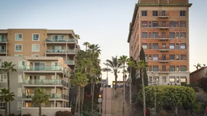 Vintage multi-story brick apartment building and modern concrete and glass apartment building separated by a steep public stairway in Los Angeles, California.