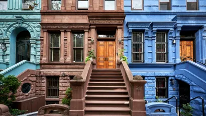 Colorful teal, brown, and blue brownstones in New York City with wide stone stairways going up to first floor doors.