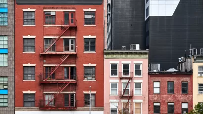 Three brick apartment buildings of various heights with fire escapes in New York City.