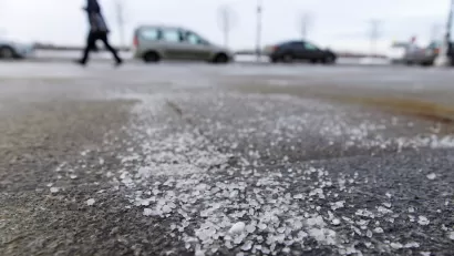 Low close-up of salt sprinkled on asphalt road in winter with person walking and car in background.