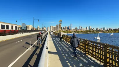 View of Boston skyline from Longfellow Bridge with cyclist riding in bike lane and pedestrian on sidewalk.