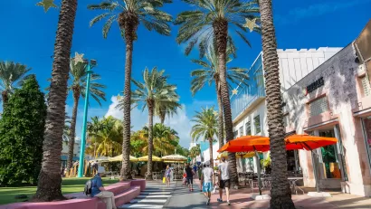 Pedestrian street with colorful patio umbrellas and tall palm trees in Miami, Florida.
