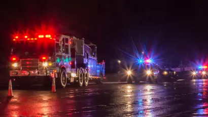 Nighttime view of fire truck and police cars with flashing lights on parked in a wet street