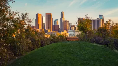 View of downtown Los Angeles at golden hour from top of grassy hill with wooden bench in Vista Hermosa Natural Park