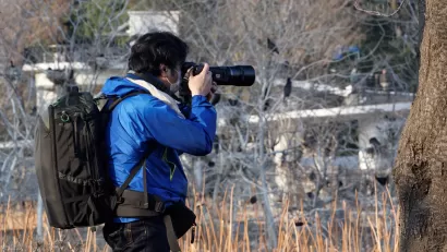 Man in blue jacket photographs birds outdoors with zoom lens
