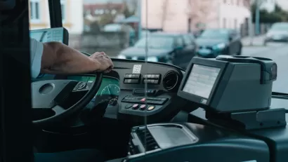 CLose-up of bus driver from behind with only hand on steering wheel visible.