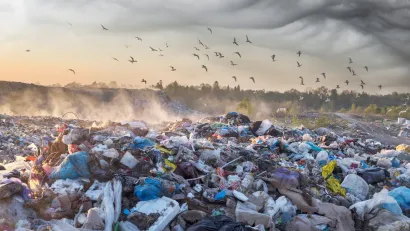 Large pile of unsorted garbage in landfill with birds flying above at sunrise or sunset.