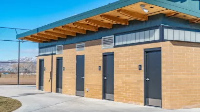 Row of four public restrooms outdoors with snowy mountain in background.
