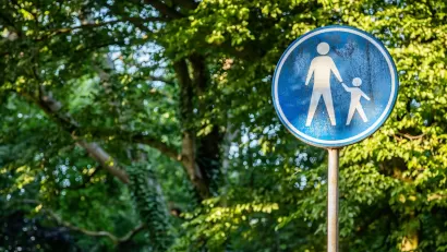 Blue sign with white sillhouettes indicating parent and child crossing street.