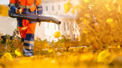 Low shot of worker in orange pants using leaf blower on yellow leaves.