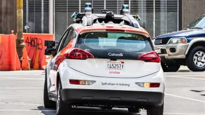 White and red Cruise self-driving car with "Self-driver in training" sign on back