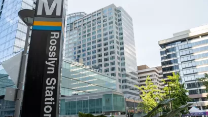 Close-up of Metro sign column at Rosslyn Station in Alexandria, Virginia with high-rose glass buildings in background.