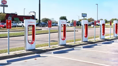 White and red Tesla EV chargers in an open-air parking lot in Corsicana, Texas with Dairy Queen restaurant in background