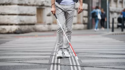 Low view of person with vision impairment cane walking through crosswalk.