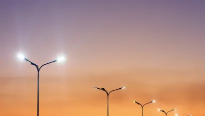 Row of double-headed street lights against orange sunset sky.