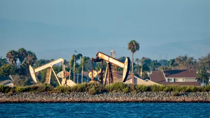Oil drilling pumps on a wetland beach in California with houses in background