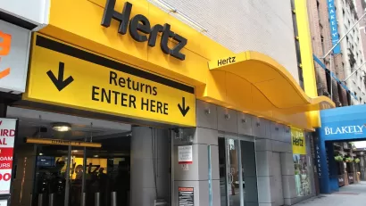 Yellow Hertz rental car log above sign "Returns ENTER HERE" and arrow above urban garage entrance.