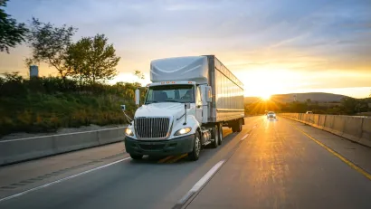 White freight truck on asphalt highway with sunset in background.