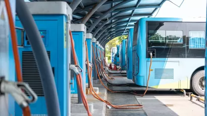Row of blue electric buses parked and plugged in at charging station.