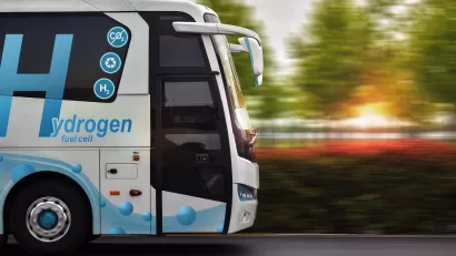Side view of white bus with blue hydrogen fuel logo driving down the street.