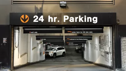 24-hour parking sign above parking garage entrance through which you can see a white SUV driving