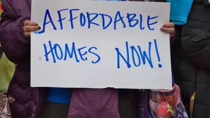 Close-up of person holding hand-written "Affordable Homes Now!" sign.