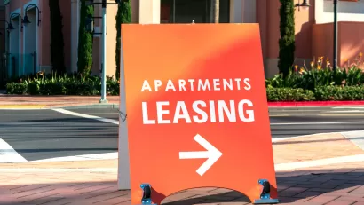 Orange "Apartments Leasing" sandwich board sign on sidewalk with arrow pointing right.