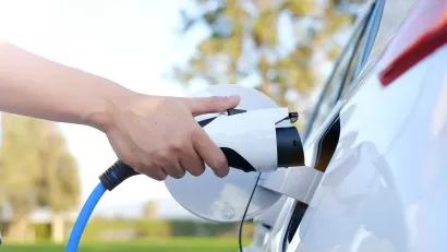 Close-up of hand holding charging cable moving toward charging port on electric car.