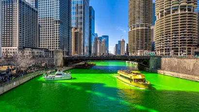 A boat floats on a bright green Chicago River lined by skyscrapers.