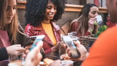 Close-up on group of young people sitting at a table using their cell phones.