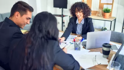 Couple on one side of desk with banker on other side looking at paperwork.