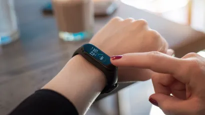 Close-up of wrist with smart watch and other hand reaching for display.