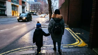 View from back of woman and child walking on London street wearing warm clothes with a black cab visible in background.
