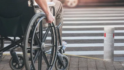 Close-up of man in manually operated wheelchair waiting at urban crosswalk.