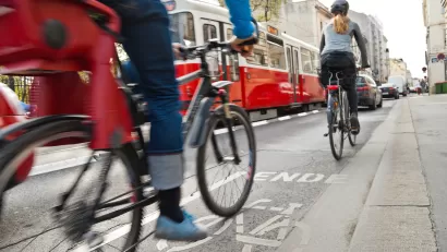 Cyclists in bike lane with red streetcar in background on urban street.