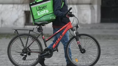 Person walking red bicycle with green Uber Eats delivery bag on cobblestone street in Bucharest, Romania.
