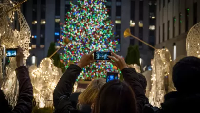 Tourists holding up cameraphones taking photos of Rockefeller Center Christmas tree in New York City.