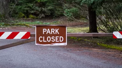 Brown "Park Closed" sign on metal swing gate outdoors.