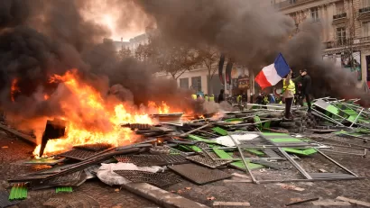 Person stands next to pile of burning debris in street holding French flag during Yellow Vest protests