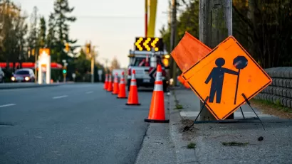 Orange sign and traffic cones indicating work zone on road.