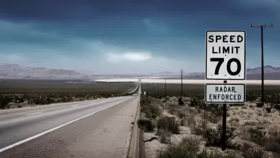 70 mph speed limit sign with bullet holes on southwestern highway with desert mountains in background.