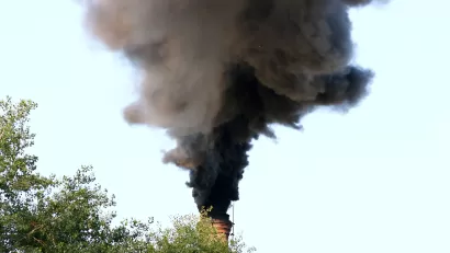 A factory smoke stack billows out black smoke into a blue sky.