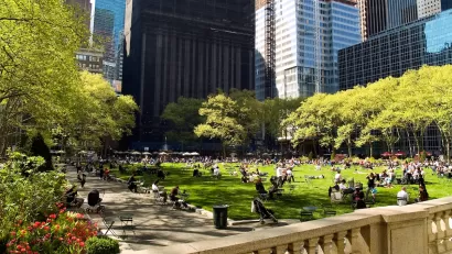 Green lawn in city park full of people sitting on lawn chairs with urban high-rises in background.