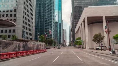 Large brutalist building and skyscrapers viewed from middle of wide street in downtown Houston, Texas.