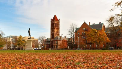 John Bridge Monument (also known as The Puritan), in the northeast corner of the Cambridge Common in Cambridge, Massachusetts with fall foliage on ground.