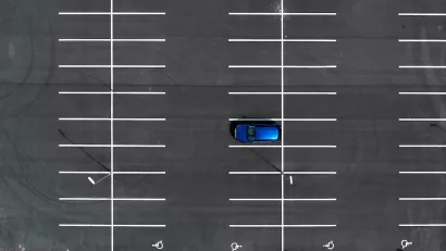 Bird's eye view of empty asphalt parking lot with one blue car.
