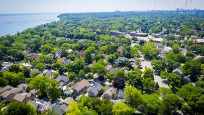 Aerial view of large homes surrounded by mature trees with Lake MIchigan shoreline at left.